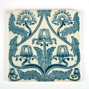 May include: A square ceramic tile featuring a symmetrical blue and white botanical pattern. The design displays stylised flowers and leafy stems arranged in a repeating motif across the off-white surface, creating a balanced and intricate visual composition.