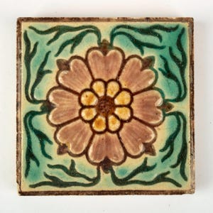 May include: Square ceramic tile with a floral design. The tile features a central flower with pink petals and a yellow centre, surrounded by green leaves on a light green background. The edges are a darker brown.