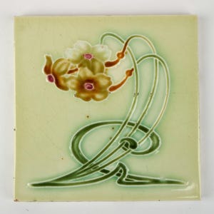 May include: Square ceramic tile with a floral design. The tile has a pale green background with a stylized floral motif in shades of green, brown, and cream. The design features curved lines and flower shapes.