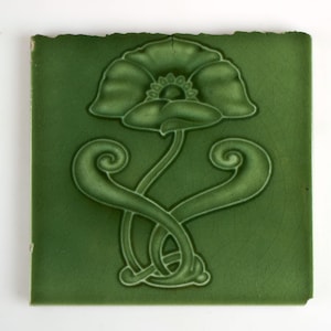 Könnte beinhalten: Eine grüne Keramikfliese mit einem erhabenen Design einer stilisierten Mohnblume mit wirbelnden Stielen.