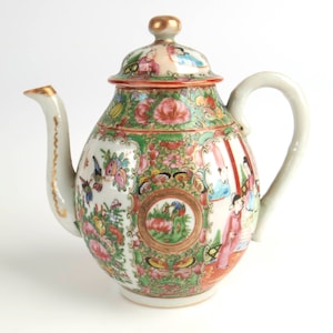 May include: A white porcelain teapot with a green, pink, and gold floral design. The teapot has a round body and a lid with a knob. The design features flowers, birds, and figures.