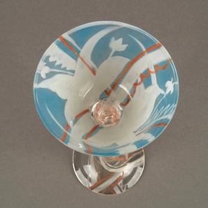 May include: A clear glass goblet with a blue and white frosted design. The goblet has a stem and a round base. The design features stylized flowers and leaves in white against a blue background. There are orange lines and swirls throughout the design.