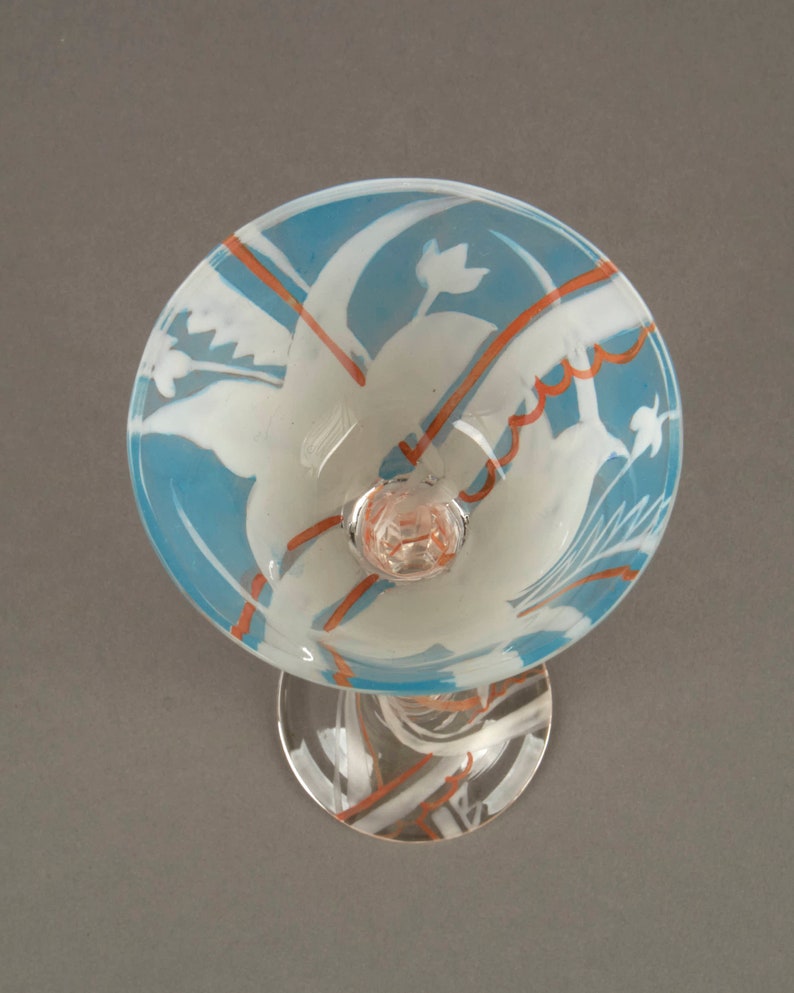 May include: A clear glass goblet with a blue and white frosted design. The goblet has a stem and a round base. The design features stylized flowers and leaves in white against a blue background. There are orange lines and swirls throughout the design.