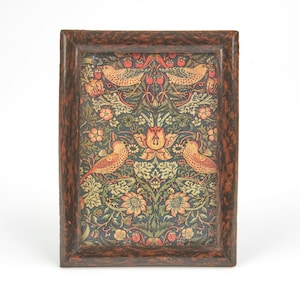 May include: A rectangular picture frame with a dark brown mottled finish containing a print featuring a symmetrical pattern of birds, flowers, and strawberries in shades of orange, green, and yellow against a dark blue background.