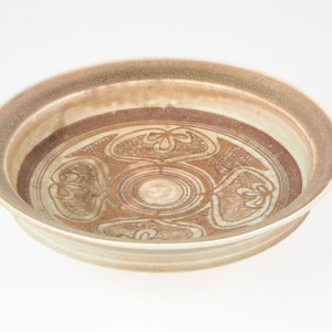 May include: A white ceramic bowl with a brown glaze and a geometric design. The bowl has a wide rim and a shallow depth.