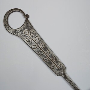 Puede incluir: Una llave de metal plateado con un dise&ntilde;o decorativo de hojas. La llave tiene un bucle en la parte superior y un eje largo y delgado.