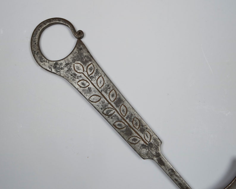 Puede incluir: Una llave de metal plateado con un dise&ntilde;o decorativo de hojas. La llave tiene un bucle en la parte superior y un eje largo y delgado.