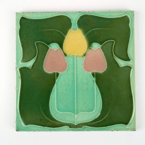 May include: Square ceramic tile with a floral design. The tile features a central motif of a yellow flower flanked by two pink buds, set against a light green background. The border is a darker shade of green, creating a contrasting frame.