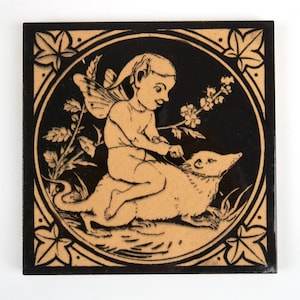 May include: Square tile with a black background and a tan illustration of a fairy riding an animal. The fairy has wings and is holding a leash. The tile is framed with a tan border featuring leaf designs.