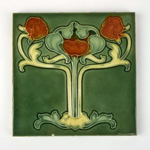 Può includere: Piastrella quadrata in ceramica verde con un motivo floreale. La piastrella presenta uno stelo centrale con foglie e fiori stilizzati nei toni del rosso, verde e giallo. Lo sfondo è verde scuro.