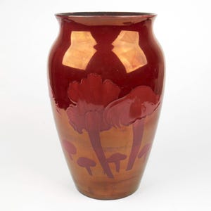 May include: A large, decorative vase with a glossy, reddish-brown finish. The vase features a design of stylized red flowers and mushrooms. The interior of the vase is a darker shade of red, and the exterior has a gradient effect.