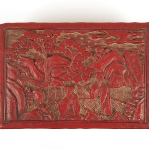 Könnte beinhalten: Eine rote lackierte Box mit aufwendigen Schnitzereien einer Landschaftsszene mit Figuren und Bäumen. Die Box ist aus Holz und hat eine rechteckige Form.