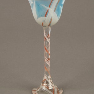 May include: A tall, clear glass goblet with a wide, flared top. The top of the goblet is decorated with a blue and white swirl pattern, and the stem is decorated with a red and white swirl pattern.