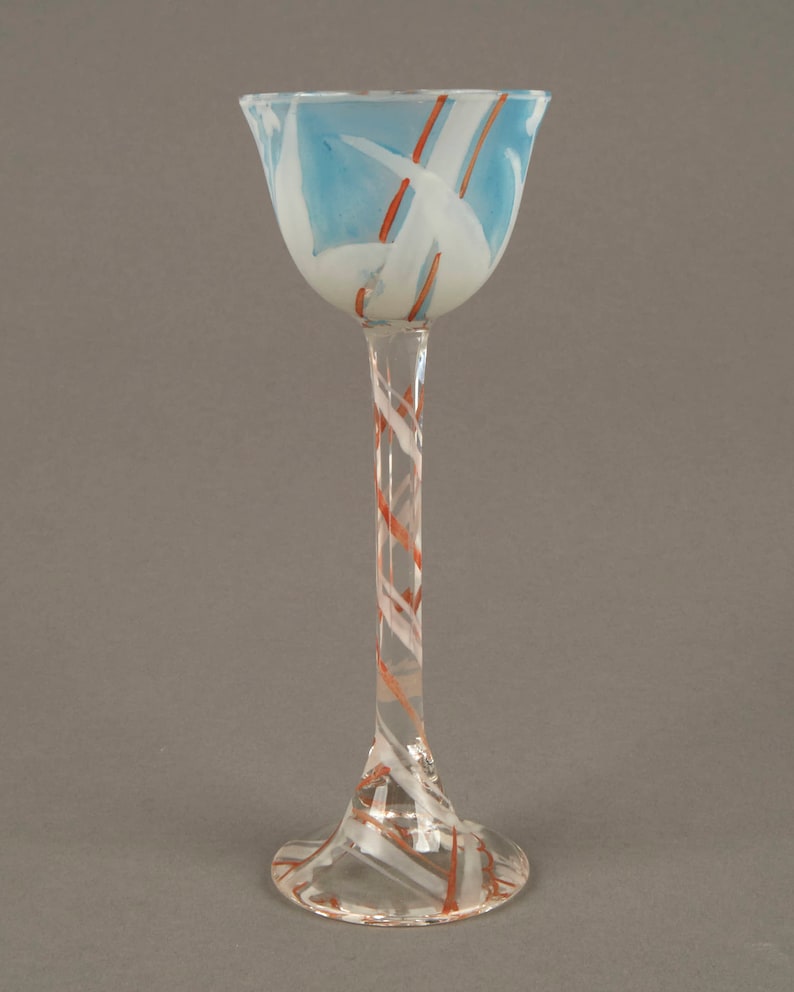 May include: A tall, clear glass goblet with a wide, flared top. The top of the goblet is decorated with a blue and white swirl pattern, and the stem is decorated with a red and white swirl pattern.