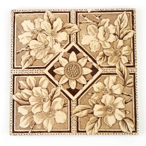 May include: A vintage ceramic tile with a brown and white floral design. The tile features a repeating pattern of stylized flowers with intricate details.