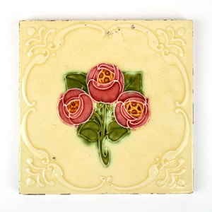 以下が含まれることがあります： 明るい黄色の背景と装飾的なボーダーが付いた正方形のセラミックタイル。 タイルの中央には、緑の葉が付いた3つの赤いバラがあります。 バラには黄色の中心があります。 ボーダーには、浮き彫りの装飾的なデザインがあります。