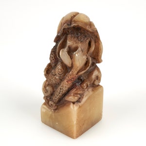 May include: A carved stone sculpture of a fish with a leafy design. The sculpture is a light brown colour and has a square base.