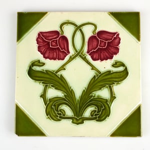May include: A vintage ceramic tile with a green and white background and a floral design. The design features two red flowers with green leaves and stems.