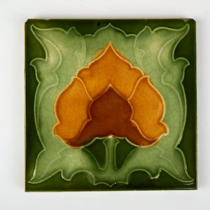 Peut inclure: Carreau de céramique carré avec un motif floral. La tuile présente une fleur centrale dans des tons orange et marron, entourée de feuilles vertes et d'une bordure vert foncé. La tuile a un glaçage craquelé.