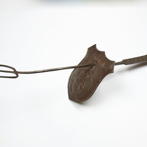 Puede incluir: Un utensilio de cocina de metal vintage con un mango largo y un tenedor de tres puntas. El utensilio tiene una cabeza en forma de escudo con la palabra "Taurus" y un dise&ntilde;o de toro estilizado.