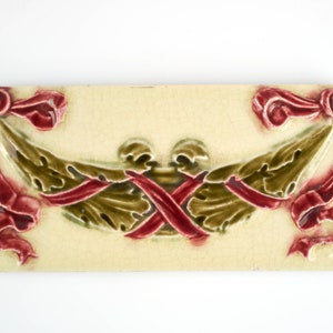 May include: A ceramic tile with a cream background and a raised design of two green leafy branches tied together with red ribbons.