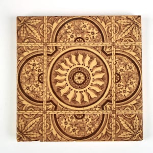 May include: A square ceramic tile featuring a dark brown and cream colour scheme. The design includes a central circular medallion with radiating petals, surrounded by four semi-circular floral motifs and corner leaf patterns within a grid.