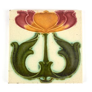 May include: A square ceramic tile with a cream-coloured background featuring a central floral motif. The design displays a stylised orange and deep red flower blossom atop a green stem, flanked by two symmetrical, curved green leaves.