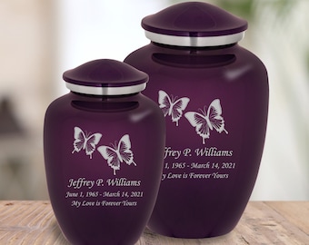 May include: Two purple cremation urns with silver lids and butterfly engravings. The urns are personalized with the name "Jeffrey P. Williams" and dates. The text "My Love is Forever Yours" is engraved on both urns.
