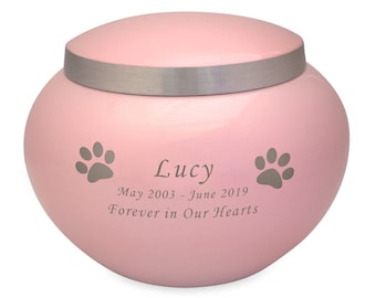 May include: Pink ceramic pet urn with a silver lid. The urn has two paw prints and the text "Lucy May 2003 - June 2019 Forever in Our Hearts".