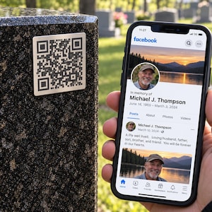 May include: A black smartphone displaying a Facebook memorial page for Michael J. Thompson, featuring a sunset lake profile photo. Beside the phone, a square QR code plaque is mounted on a dark, speckled granite surface, likely a headstone.
