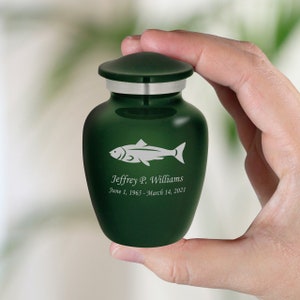May include: A dark green cremation urn with a silver lid. The urn is engraved with a fish and the text "Jeffrey P. Williams June 1, 1965 - March 14, 2021".