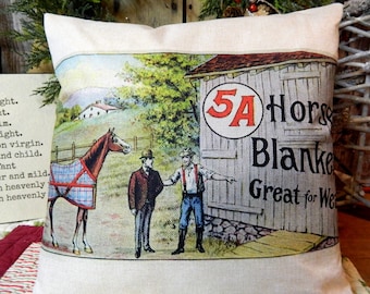 May include: A rectangular pillow with a vintage illustration. The image depicts a horse wearing a blanket, two men, and a barn with the text "5A Horse Blanket Great for Wear". The pillow has a cream-colored background.