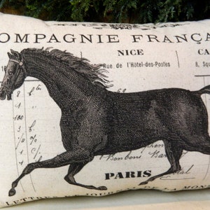 May include: Rectangular pillow with a black horse illustration. The pillow features French text, including "COMPAGNIE FRAN&Ccedil;AISE," "NICE," "CANNES," and "PARIS." The design has a vintage, antique aesthetic, with a cream-colored background.