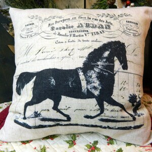 May include: A decorative pillow with a black horse silhouette and vintage French text. The pillow is beige and has a rectangular shape. The horse design is centered on the pillow, with the text above and below the horse.
