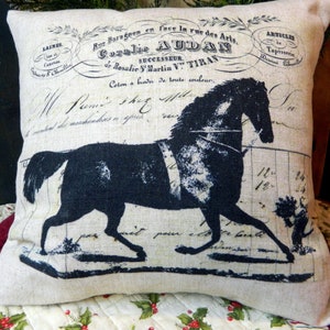 May include: A decorative pillow with a black horse silhouette and vintage French script. The pillow has a neutral linen-like background with printed text and a horse design, suitable for home decor.