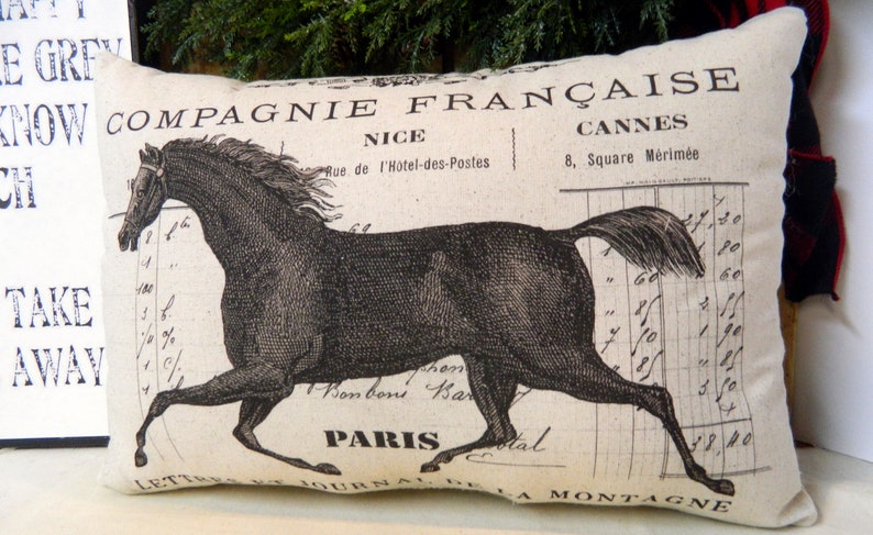 May include: Rectangular pillow with a vintage French design. The pillow features a black illustration of a running horse, with text including "Compagnie Fran&ccedil;aise" and "Paris" on a cream-colored background. The pillow has a soft, textured appearance.