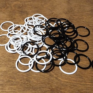 May include: A collection of white and black rubber O-rings. The O-rings are scattered on a wooden surface. The O-rings are circular and appear to be new.