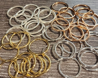 May include: A collection of thin, circular rings in gold, silver, and rose gold tones. The rings are scattered across a dark wood-grain surface, creating a visually appealing arrangement. These rings could be used for jewelry making or other craft projects.