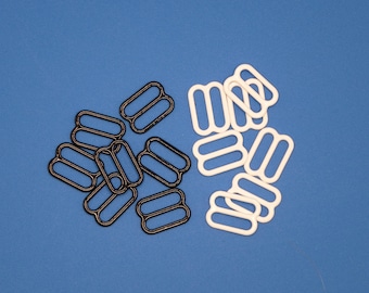 May include: A collection of black and white bra strap sliders, also known as lingerie hardware, arranged on a blue background. The sliders are made of plastic and have a rectangular shape with two parallel slots.