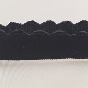 May include: Close-up of a black scalloped trim. The trim has a velvet-like texture and a decorative, wavy edge. This trim is suitable for various sewing and crafting projects.
