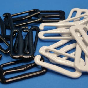 Peut inclure: Gros plan sur des agrafes de soutien-gorge noires et blanches. Les agrafes sont en matériau brillant et disposées de manière éparse. Les agrafes ont un design incurvé et sont de différentes formes et tailles.