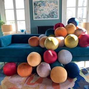 May include: A teal velvet sofa with a variety of colorful round pillows in shades of yellow, orange, red, purple, and blue. The pillows are arranged in a pile on the sofa.