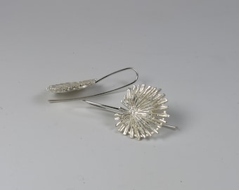 May include: A pair of silver dangle earrings with a unique, textured, organic design. The earrings are made of a delicate, wire-like material that creates a flowing, asymmetrical shape.