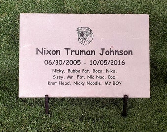 May include: A gray stone memorial with a black and white image of a bulldog. The text reads "Nixon Truman Johnson 06/30/2005 - 10/05/2016 Nicky, Bubba Fat, Bozo, Nixa, Sissy, Mr. Fat, Nic Nac, Boz, Knot Head, Nicky Noodle, MY BOY"