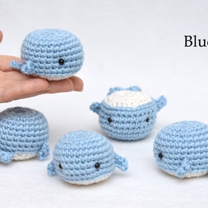 May include: Five crocheted whale plushies in blue and white. The whales have black eyes and are arranged on a white surface. Blue.