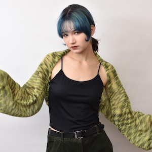 May include: A black spaghetti strap tank top paired with a lime green and dark olive green variegated knit shrug featuring long, wide sleeves. The shrug has a loose, open-front design that drapes across the shoulders and arms, showcasing a textured knit pattern.