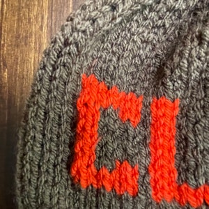 May include: A gray knitted hat with the letter "C" knitted in orange.