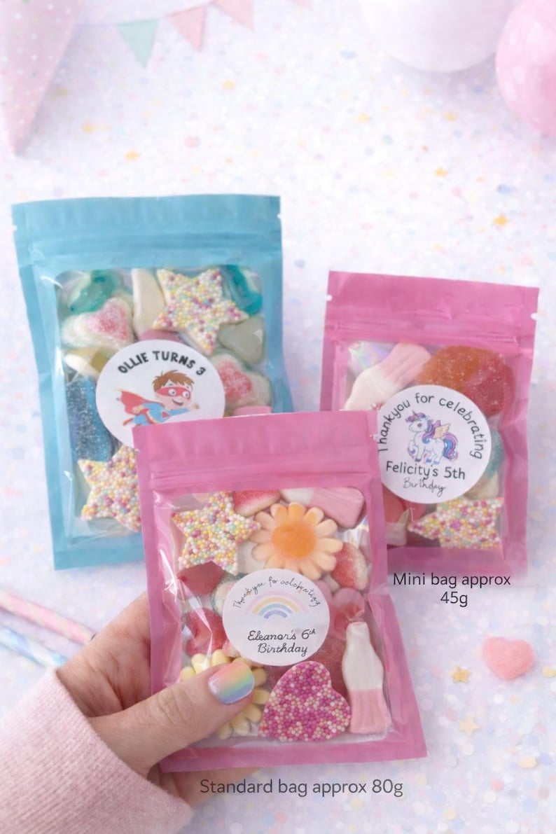 K&ouml;nnte beinhalten: Drei wiederverschlie&szlig;bare Kunststoffbeutel gef&uuml;llt mit verschiedenen Fruchtgummis. Ein blauer Beutel mit der Aufschrift Ollie Turns 3, ein rosa Beutel mit der Aufschrift Thank you for celebrating Felicity's 5th Birthday und ein rosa Beutel mit der Aufschrift Thank you for celebrating Eleanor's 6th Birthday.