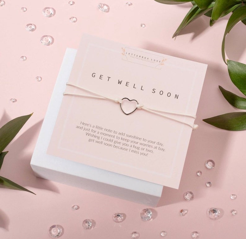 May include: White string bracelet with a silver heart charm and a card that reads "Get Well Soon" with a message of encouragement.