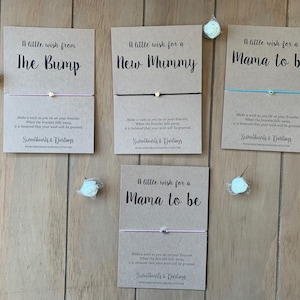 May include: Four cards with a wish bracelet attached to each. The cards are brown and have white text. The text on the cards reads "A little wish from The Bump", "A little wish for a New Mummy", "A little wish for a Mama to be", and "A little wish for a Mama to be".